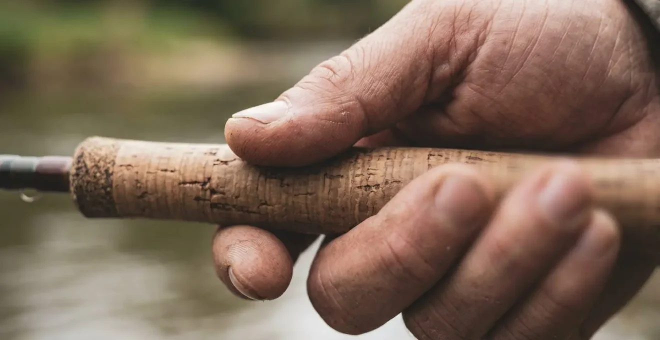 Gros plan sur les mains d'un pêcheur tenant une canne, captant les vibrations subtiles dans l'eau